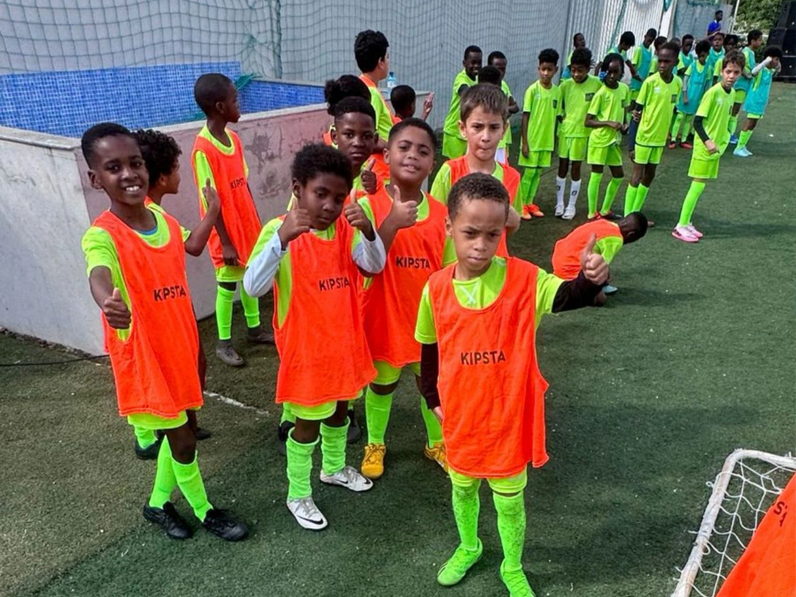 Crianças da escola de futebol com equipamento verde e coletes laranja no Decifer